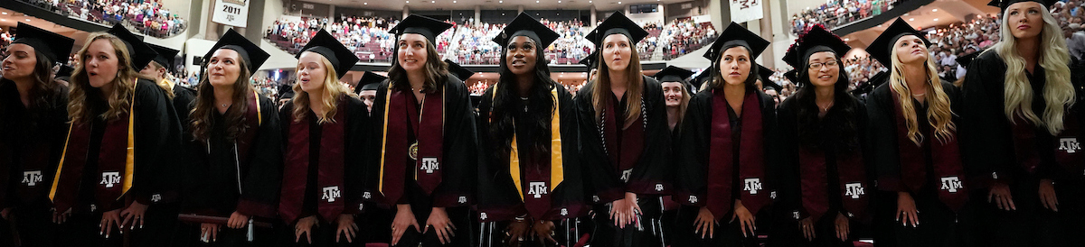 Students in caps and gowns singing the Aggie War Hymn at graduation