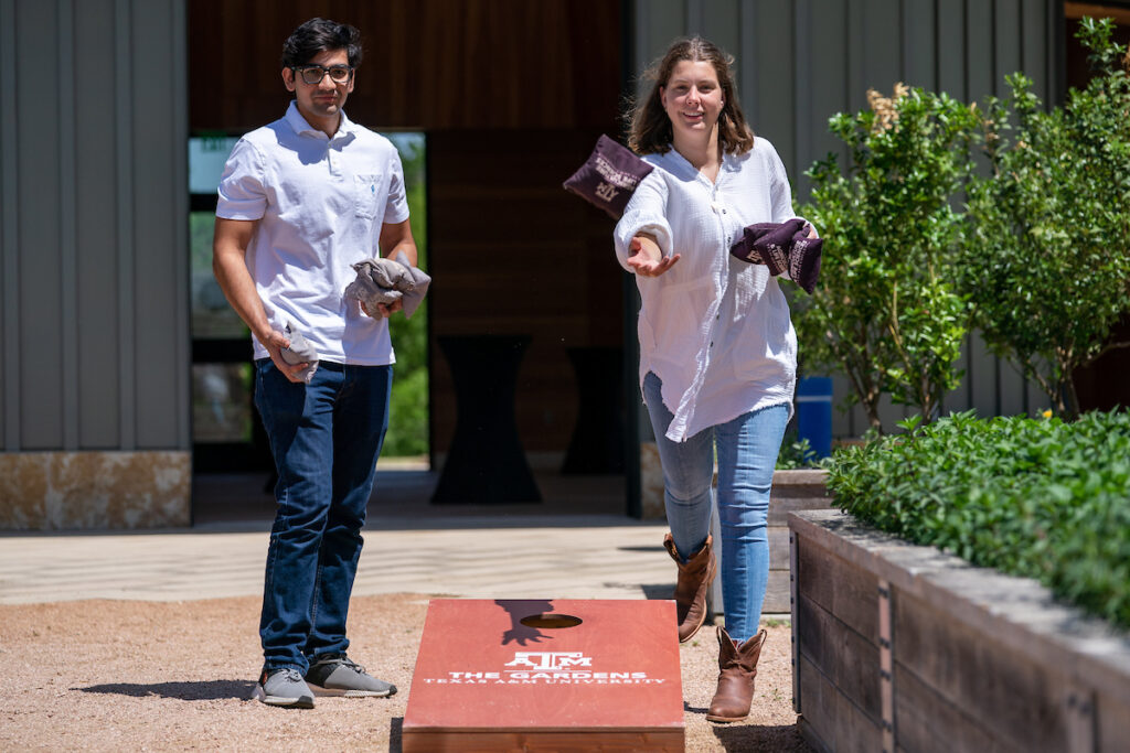 two students playing cornhole at an event in The Gardens