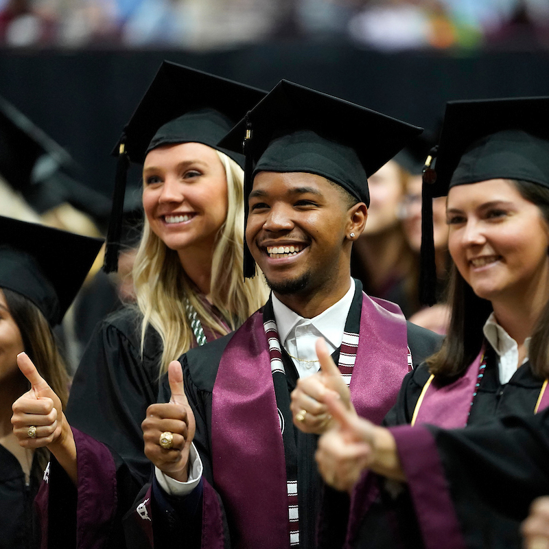 students at Texas A&M University commencement ceremony giving thumbs up
