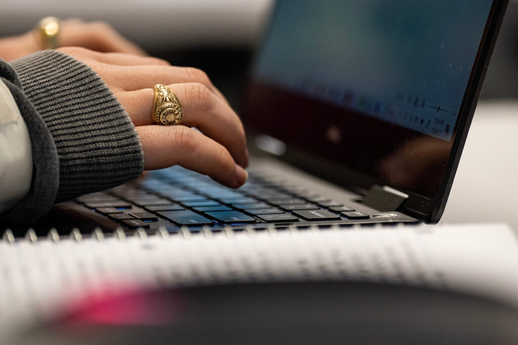 Close-up of a person with an Aggie Ring typing on a laptop